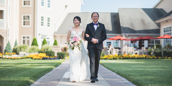 A bride walks down the wedding aisle at The Lodge at Geneva-on-the-Lake with her father